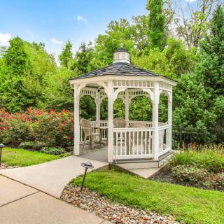 A charming white gazebo surrounded by lush greenery in a garden setting.