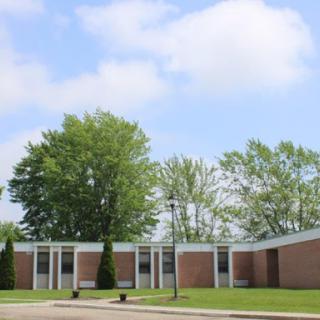 A school building surrounded by greenery under a partly cloudy sky.