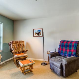 A cozy living room corner with an armchair, rocking chair, and a soft lamp.
