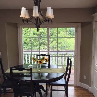 A cozy dining area with a table, chairs, and a chandelier, overlooking a lush green view through sliding glass doors.