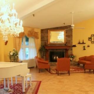 A cozy living room with a grand piano and a chandelier, featuring a fireplace and comfortable seating.