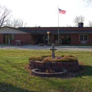 A single-story brick building with a flagpole and an American flag, surrounded by grass and a small fountain in the foreground.