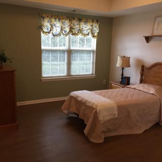 A cozy bedroom with a single bed and window, featuring a lamp and dresser.