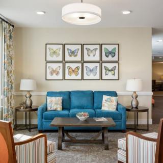 A cozy living room featuring a blue sofa, butterfly artwork on the wall, and modern decor elements like lamps and a coffee table.
