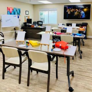 A classroom setup with desks, chairs, and training materials, featuring a whiteboard and a large television.