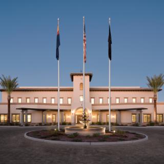 A modern building with flags and a fountain, set against an evening sky.