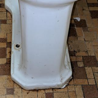 A close-up view of the base of a toilet, showing signs of wear on the surface.