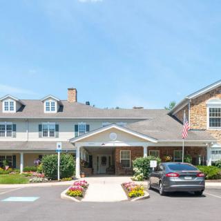 A front view of a residential building with a car parked in the driveway and flowers lining the entrance.