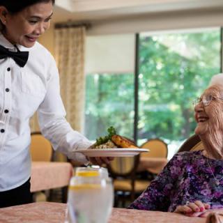 A waiter serves food to an elderly woman at a restaurant.