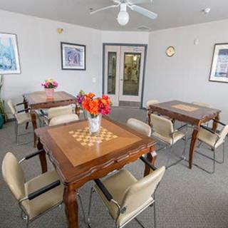 A cozy room with multiple tables featuring chess board designs, surrounded by chairs and decorated with vases of flowers.