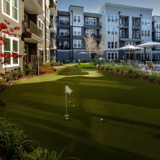 A modern apartment complex featuring a well-manicured putting green in its outdoor area.