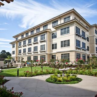 A modern multi-story building with a well-maintained garden and lawn in the foreground.