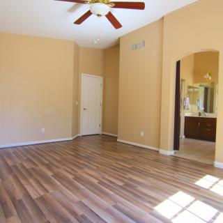 An empty room with hardwood floors and a ceiling fan, featuring beige walls and a doorway leading to another area.