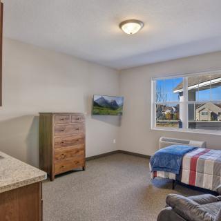 A well-lit bedroom with a single bed, dresser, and wall-mounted TV.