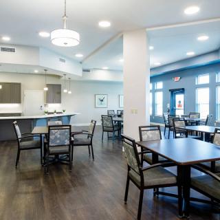 A modern dining area with tables, chairs, and a kitchen section in the background.