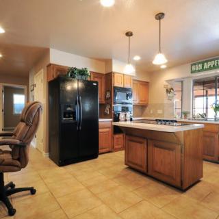 A modern kitchen with wood cabinets, a central island, black refrigerator, and overhead lighting.