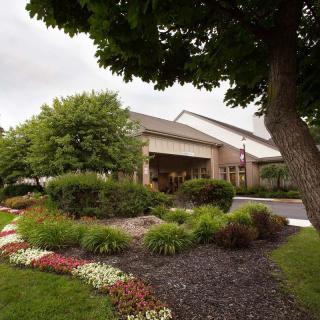 A building entrance surrounded by lush landscaping, featuring a variety of trees and colorful flowers.