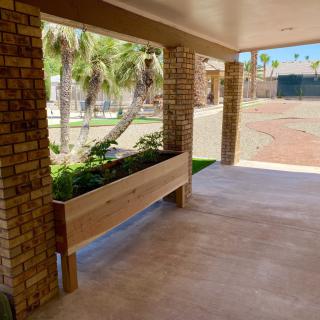 A wooden planter box filled with greenery on a covered patio with brick columns.
