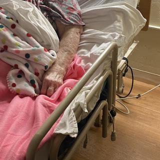 A patient's arm resting on the edge of a hospital bed, surrounded by blankets.
