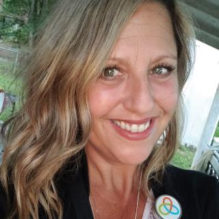 A woman smiles outdoors, wearing a button badge.