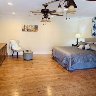 A modern bedroom featuring a king-sized bed with gray bedding, hardwood flooring, and stylish decor elements.