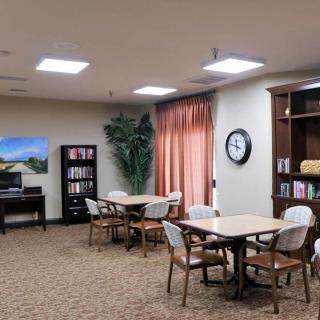 A cozy library room with tables and chairs, bookshelves, and a clock on the wall.