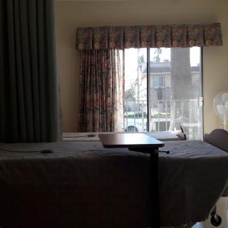 A hospital room with a bed, curtains, and sunlight streaming through a window.