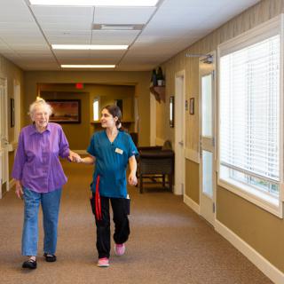 A caregiver assisting an elderly person in a nursing home hallway.