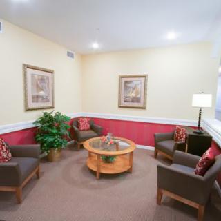 A cozy waiting room with a seating area, featuring four chairs, a round coffee table, wall art, and a potted plant.