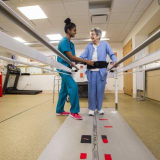 A healthcare professional assists a patient in a rehabilitation session using parallel bars.