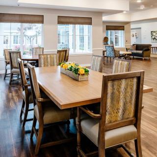 A well-lit dining room with a large wooden table and chairs, featuring a decorative centerpiece.