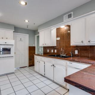 A modern kitchen featuring white cabinets, a built-in oven, and a double sink with a tiled floor.