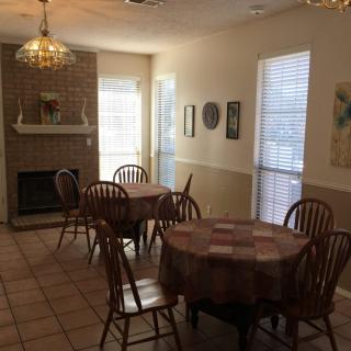 A cozy dining area featuring circular tables with chairs, a brick fireplace, and natural lighting from windows.