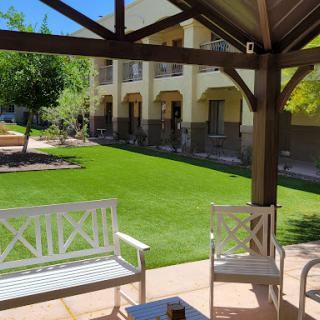 A serene outdoor patio area with white furniture, overlooking a manicured lawn and sunny surroundings.