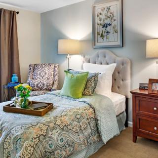 A cozy bedroom featuring a neatly made bed with patterned bedding, decorative pillows, and a wooden nightstand with lamps.