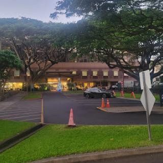 A serene view of a building surrounded by trees, featuring a parking lot and street signage in the evening light.