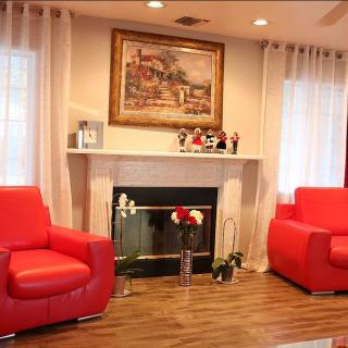 A cozy living room featuring vibrant red chairs and a fireplace, accented by a decorative painting and soft curtains.