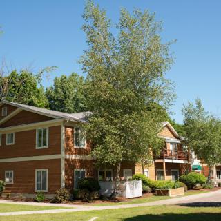 A two-story apartment building surrounded by trees on a sunny day.