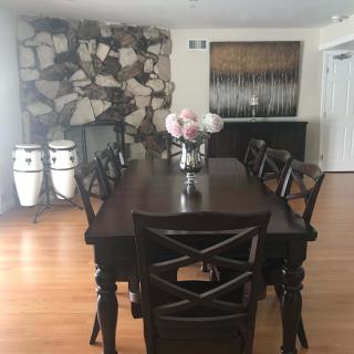 A modern dining room with a dark wood table, chairs, and decorative elements including flowers and conga drums.