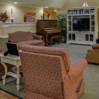 A cozy living room with a piano and television, featuring comfortable seating and warm decor.