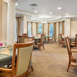 A well-furnished dining area with elegant tables and chairs, featuring warm lighting and a carpeted floor.