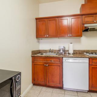 A compact kitchen area with wooden cabinets, a sink, a dishwasher, and a microwave.