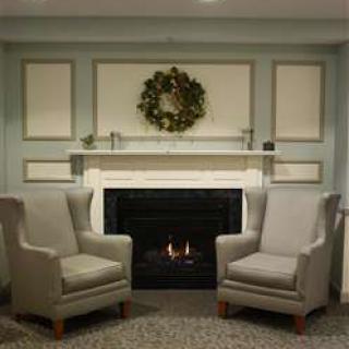A cozy living room with a fireplace, two chairs, and a decorative wreath above the mantel.