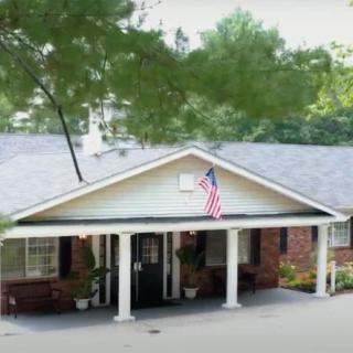 A house with a covered entrance displaying an American flag, surrounded by trees.