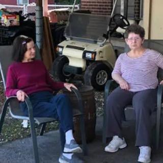 Two people sitting and conversing on a patio with a golf cart in the background.