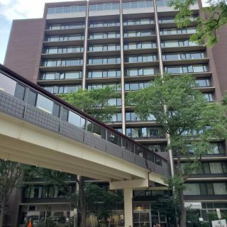 A modern multi-story building with a skywalk surrounded by trees.
