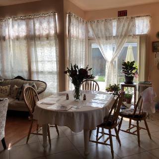 A cozy dining area with a table set near large windows draped with curtains, letting in natural light.
