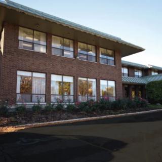A two-story brick building with large windows and a landscaped entrance.
