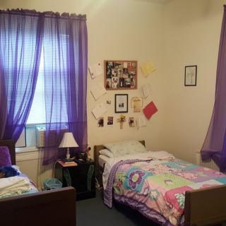 A cozy shared bedroom with purple curtains and twin beds featuring colorful bedding.