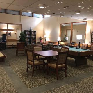 A cozy library interior with tables, chairs, and bookshelves, illuminated by warm lighting.